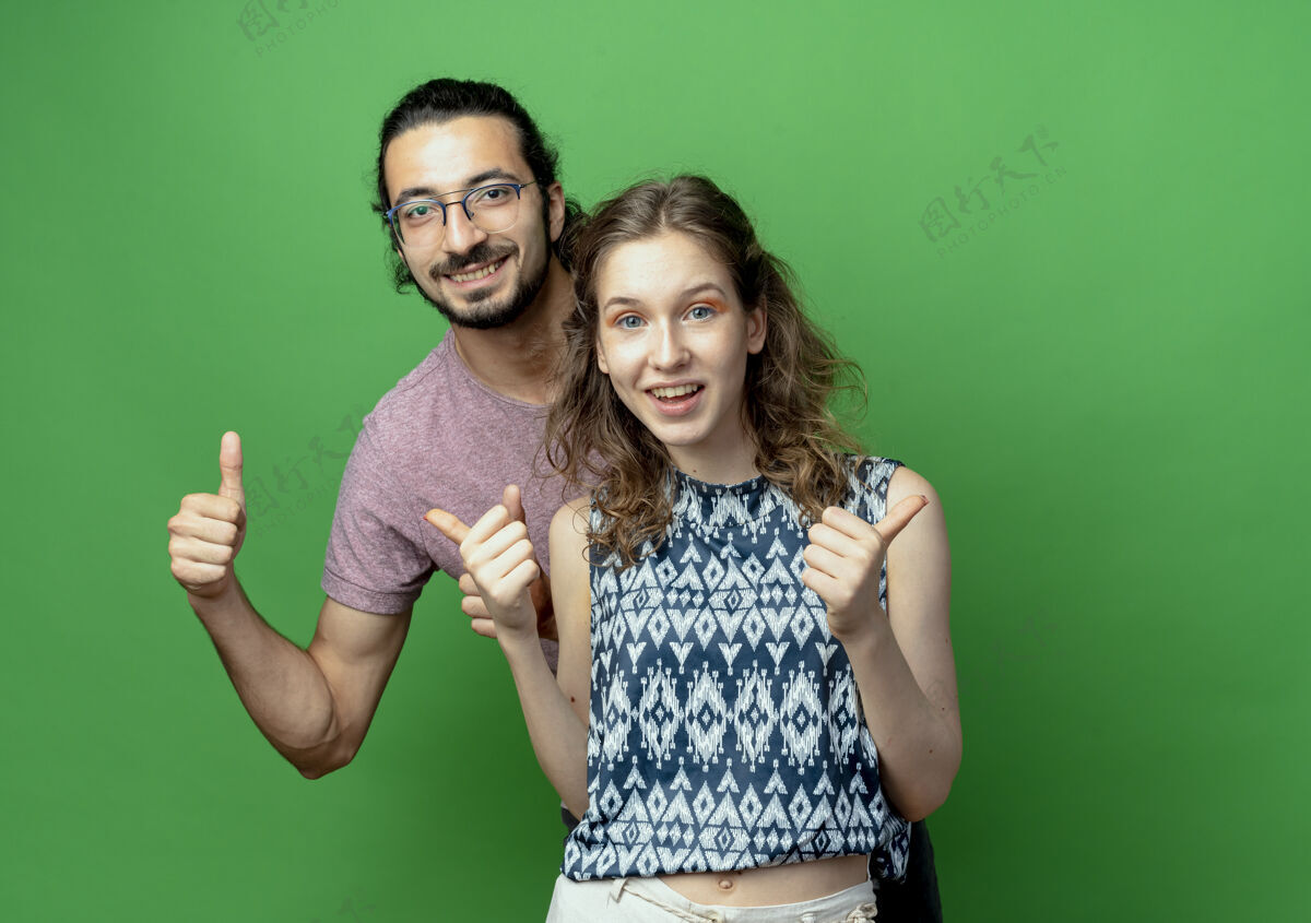 成功一对成功的年轻夫妇看着相机 在绿色的背景下愉快地竖起大拇指相机微笑欢呼