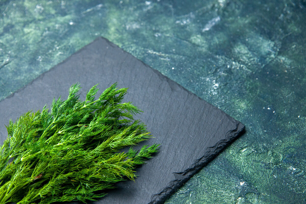 壁板新鲜莳萝束正面图 黑色砧板右侧 绿-黑混合色背景 自由空间扫帚前面草药