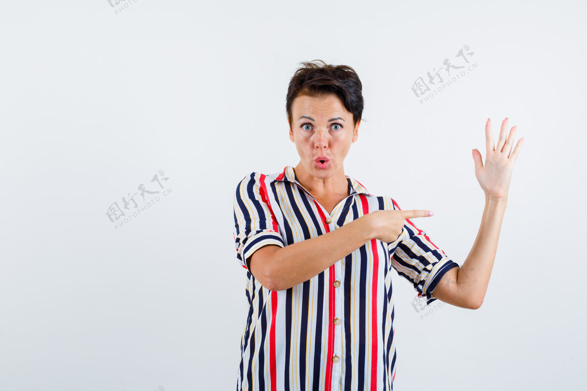 衬衫成熟的女人展示停车标志 穿着条纹衬衫指着停车标志 看起来很专注 正面视图老年人自信姿势