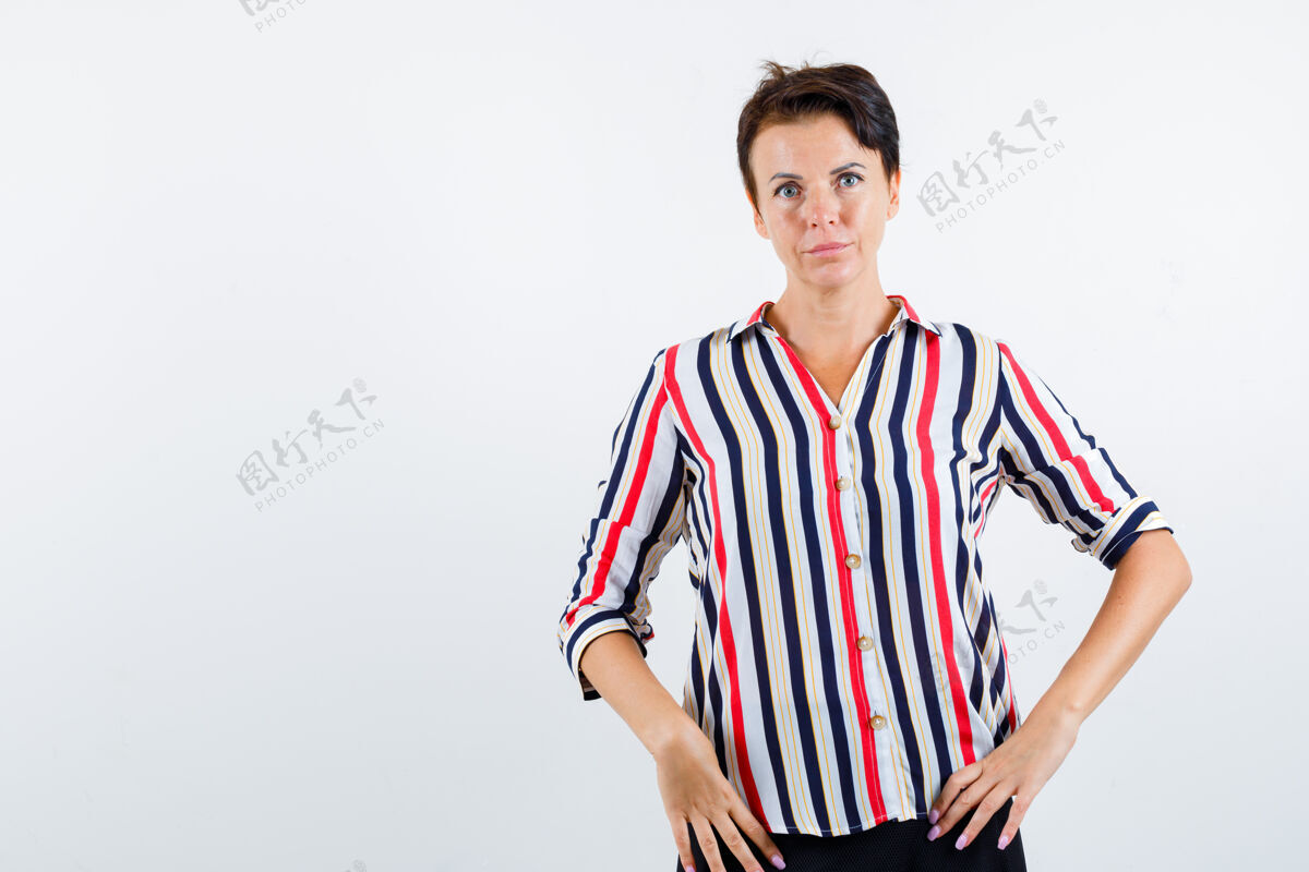 优雅穿条纹衬衫的成熟女人 手放在腰上 看起来很自信 前视图条纹姿势女士
