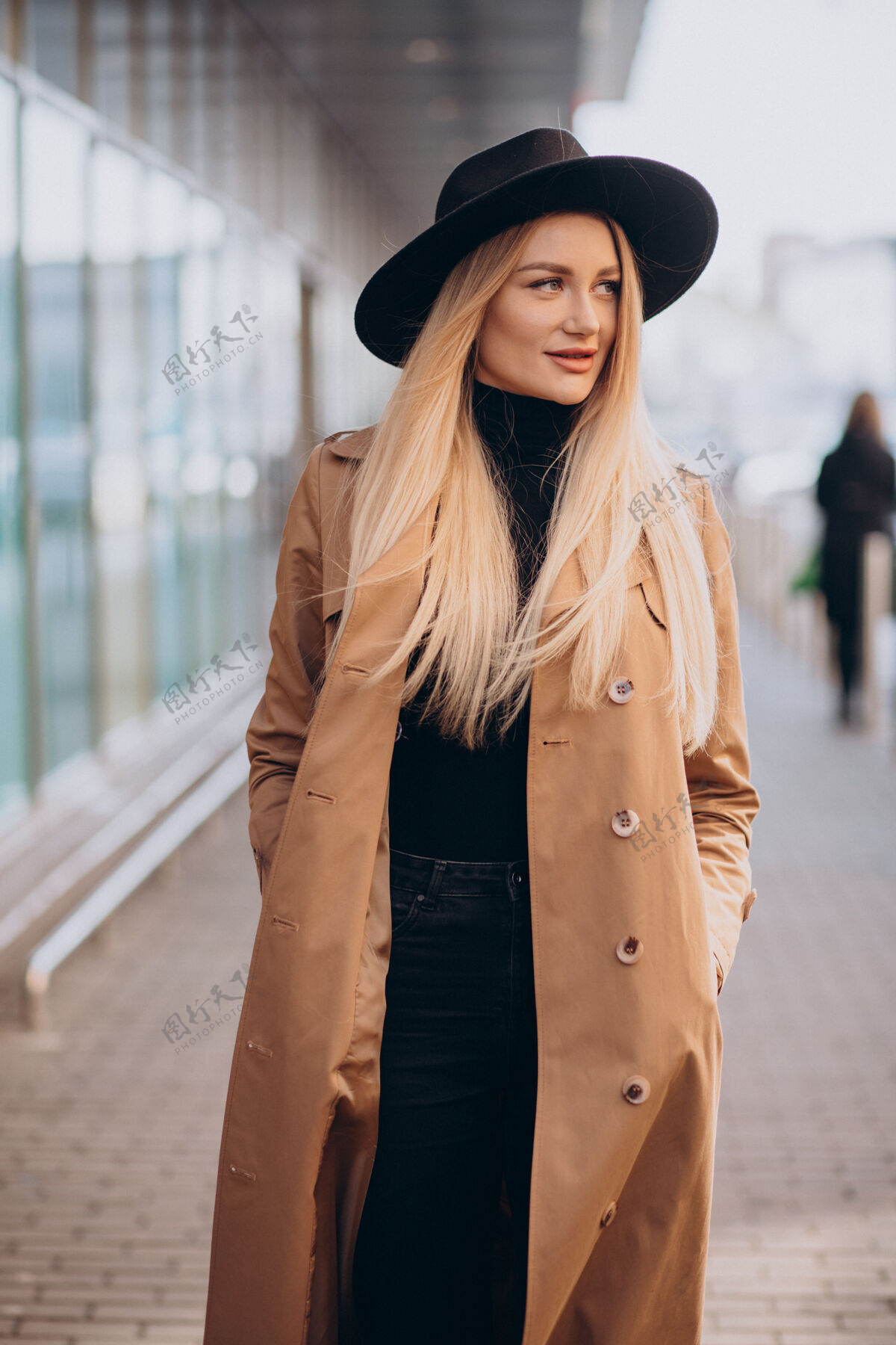 优雅戴着黑帽子 穿着米黄色外套的年轻漂亮女人走过商场姿势购物服装