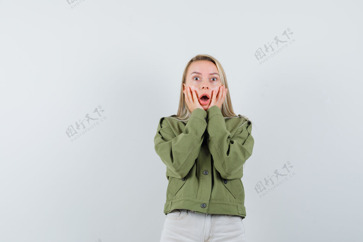 成人穿着绿色夹克的年轻女性 牛仔裤手放在脸颊上 看起来很害怕 正面视图脸肖像抱着