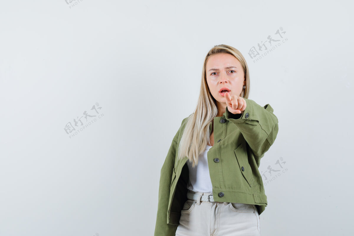 成人金发女郎穿着夹克 裤子指着摄像机 表情严肃前视图女性健康肖像