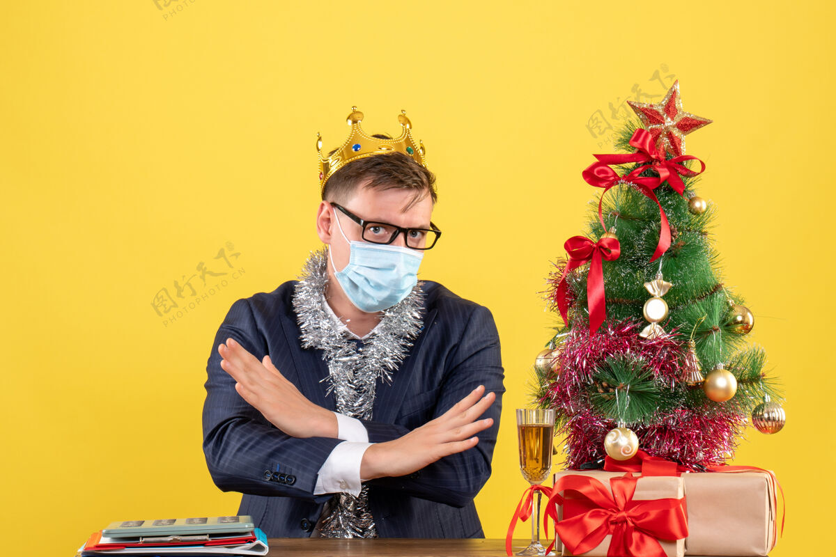 人前视图商务人士交叉双手坐在圣诞树附近的桌子上 呈现黄色背景前面头发坐着