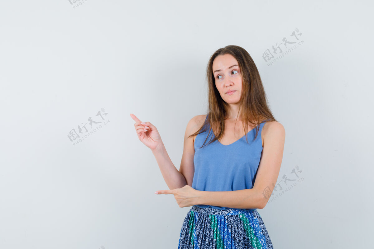 健康年轻的女士站在一边指着单打 裙子和看犹豫前视图肖像犹豫女孩