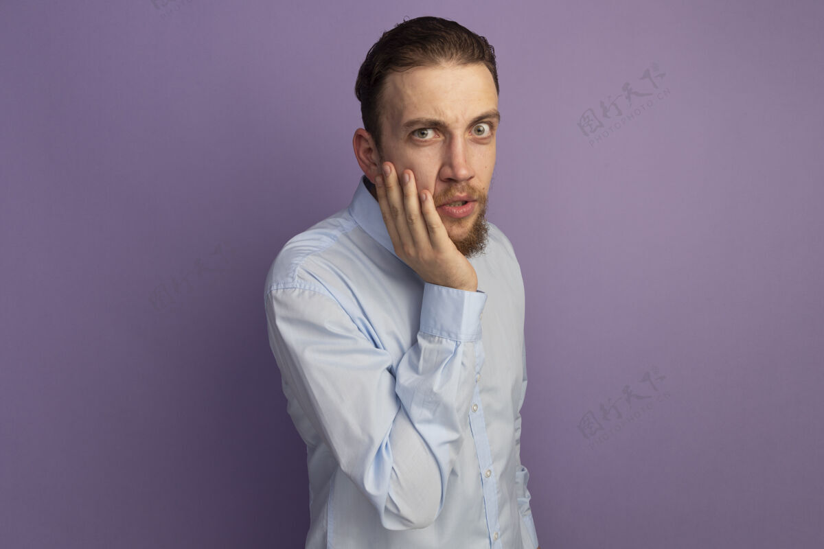 市民震惊的金发帅哥把手放在脸上 看着紫色墙壁上孤立的前方人人衣服