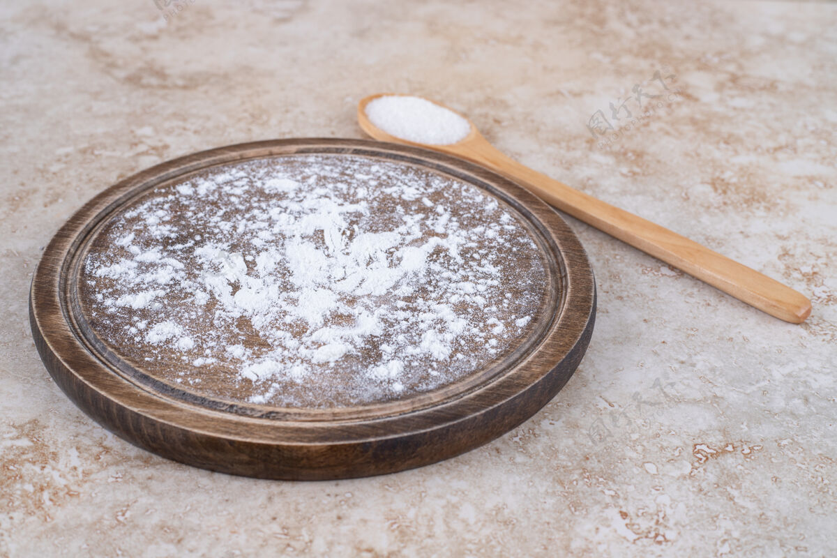 平板一盘棕色的面粉和一把木勺糖面粉有机营养