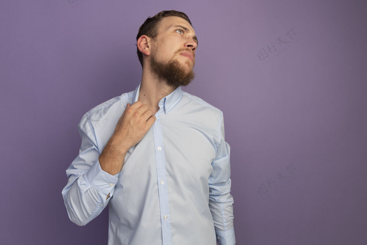 领子恼怒的金发帅哥拿着衣领 看着紫色墙上孤立的一面男人人抱着