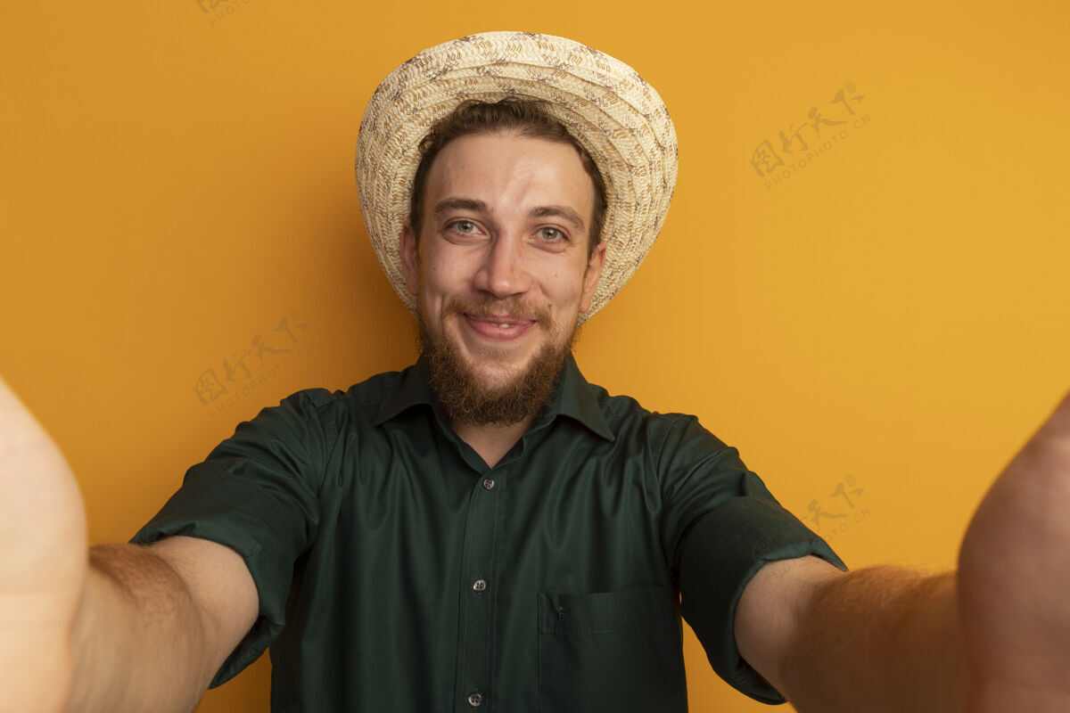 站着一个戴着沙滩帽的金发帅哥假装站在橙色的墙上孤立的站在前面人帅哥金发