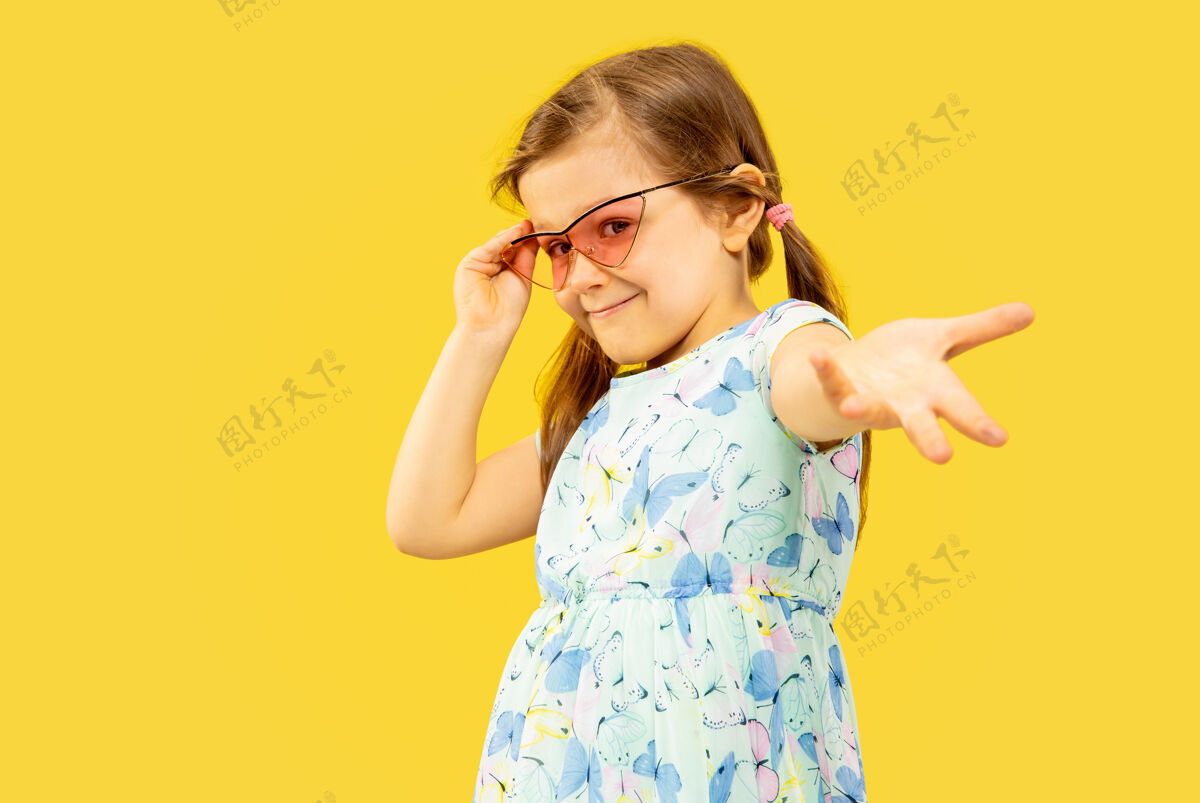 休息美丽动情的小女孩孤立在黄色背景上半幅快乐的孩子站着的肖像 穿着裙子 戴着红色太阳镜夏天的概念 人类的情感 童年青少年人肖像