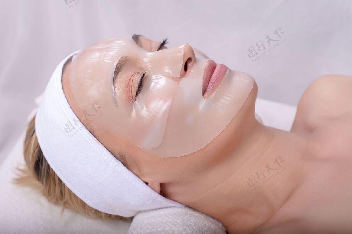 手在水疗中心脸上戴着面膜的年轻白人女性美丽放松女人