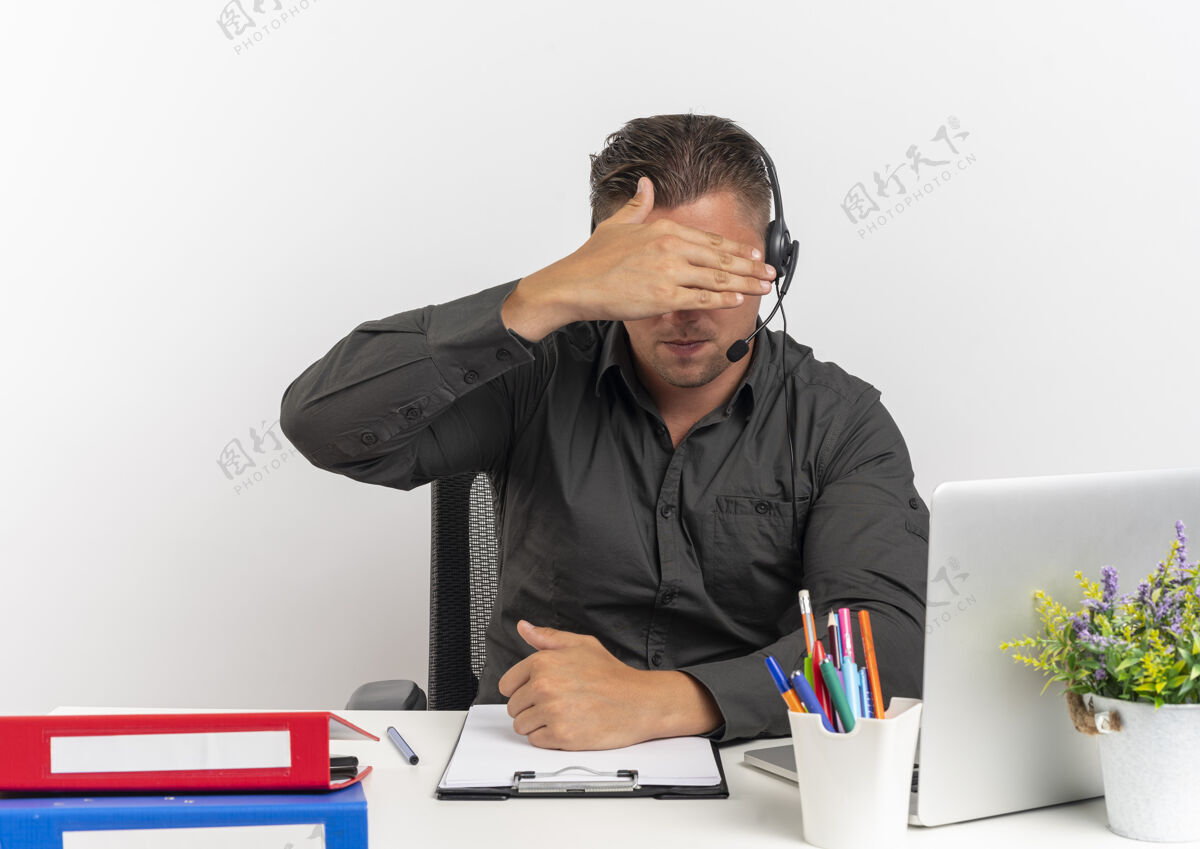 工具年轻的金发上班族戴着耳机坐在办公桌旁 拿着办公工具用笔记本电脑藏着脸 手被隔离在白色背景上 还有复印空间笔记本电脑年轻坐着