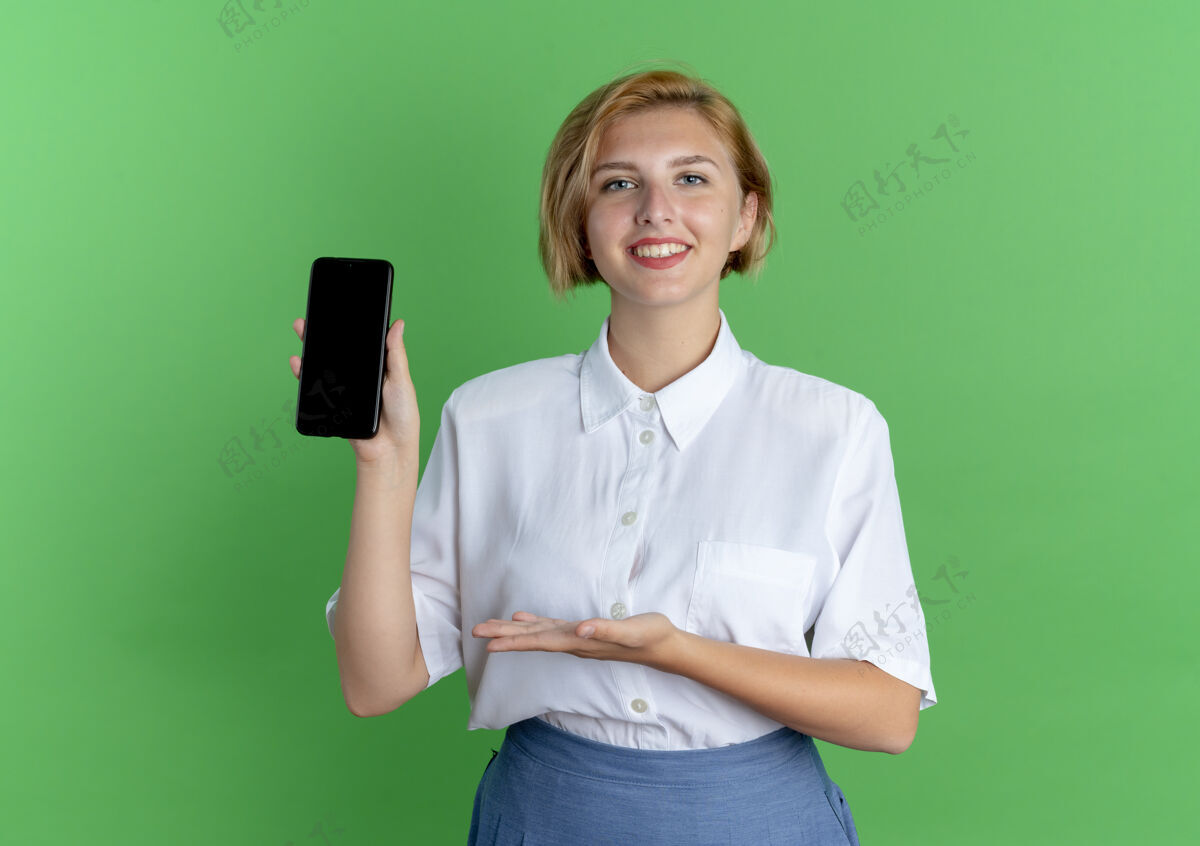 举行年轻的微笑的金发俄罗斯女孩手拿着和点在绿色背景与复制空间孤立的电话尖电话女孩