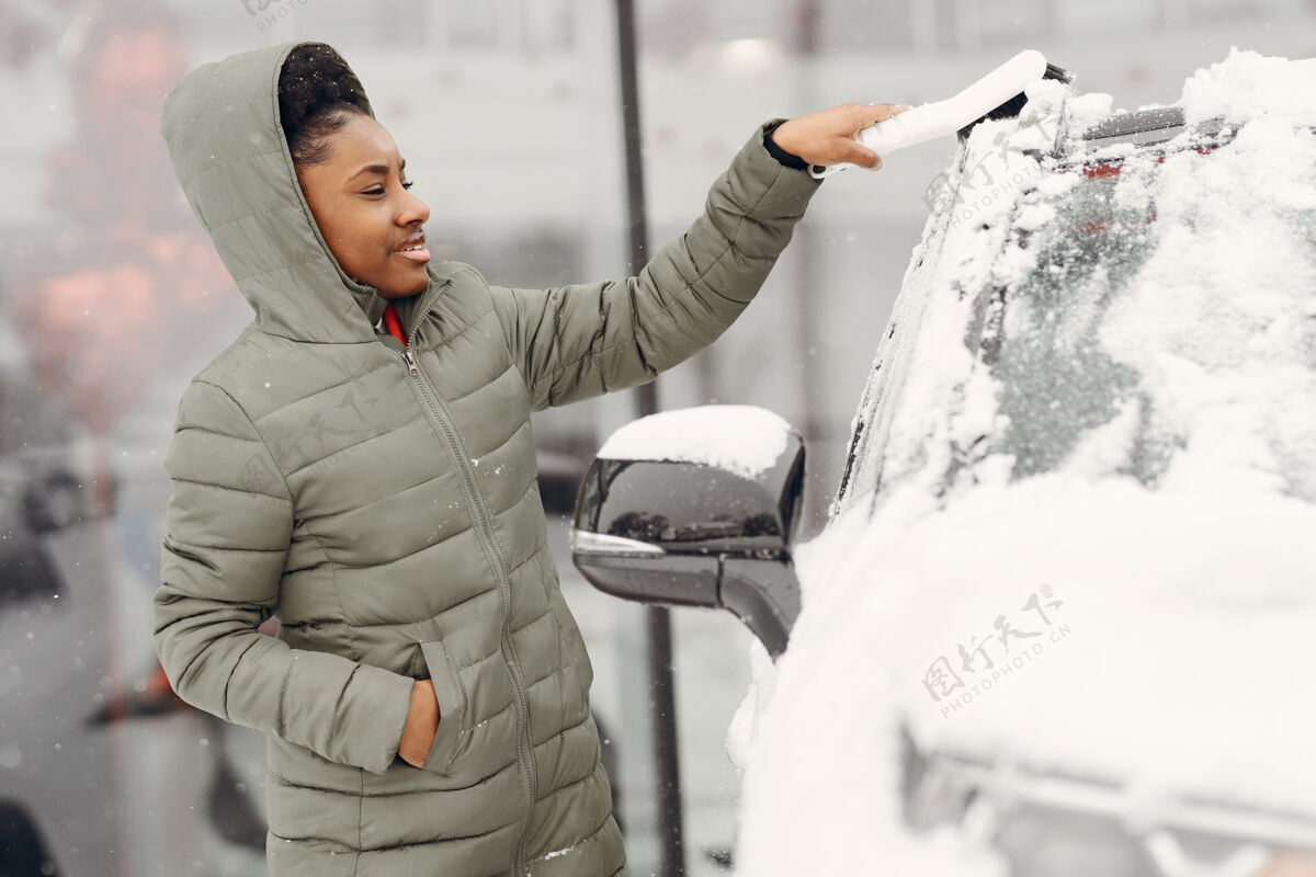 司机冬天非洲女人在车上扫雪的肖像穿着绿色夹克的女人暴风雪清洁工作