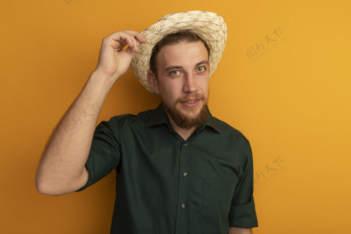 海滩自信帅气的金发男子戴着沙滩帽 看着橙色墙壁上孤立的前方表情脸市民