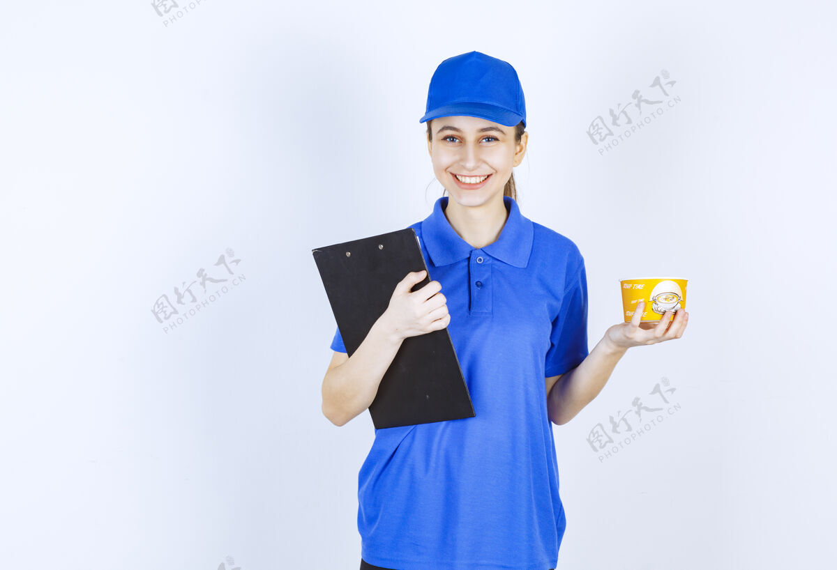 人穿着蓝色制服的女快递员手里拿着一个外卖面杯和一个黑色文件夹模特人姿势
