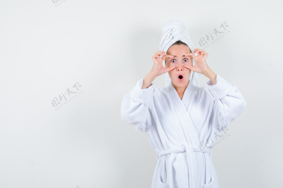 漂亮年轻女子睁开眼睛用手指在白色浴衣 毛巾和看起来震惊前视图欢呼卷发现代