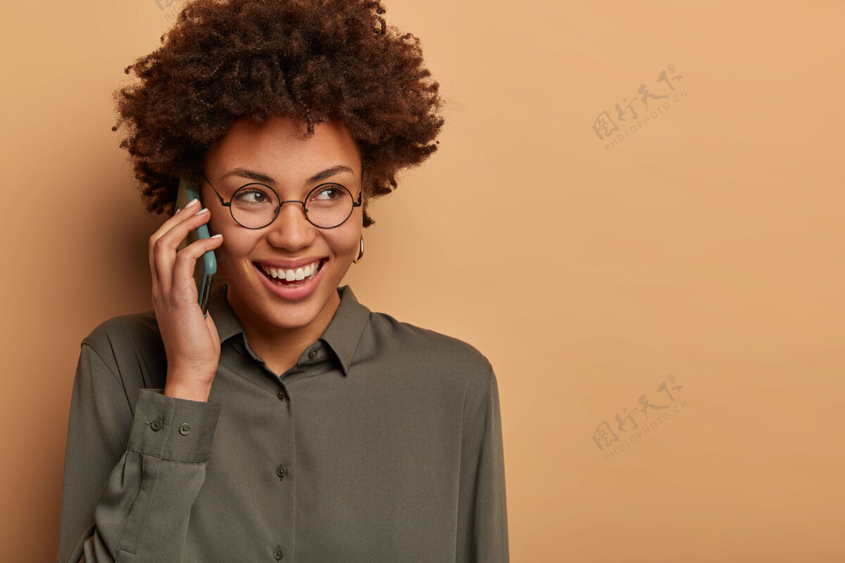 非洲人开朗的美国黑人妇女的特写镜头有搞笑的电话交谈 笑容灿烂 沉思地看着某处头发手机电话