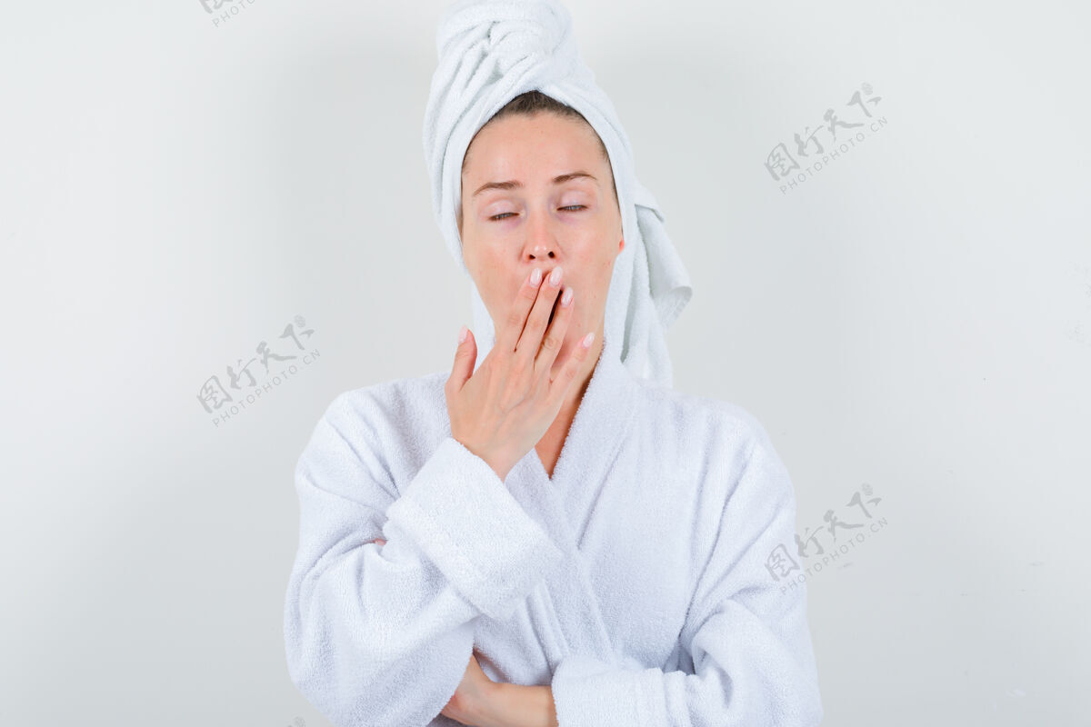 节日年轻女子打着哈欠在白色浴袍 毛巾和看起来困倦 前视图欢乐女性漂亮