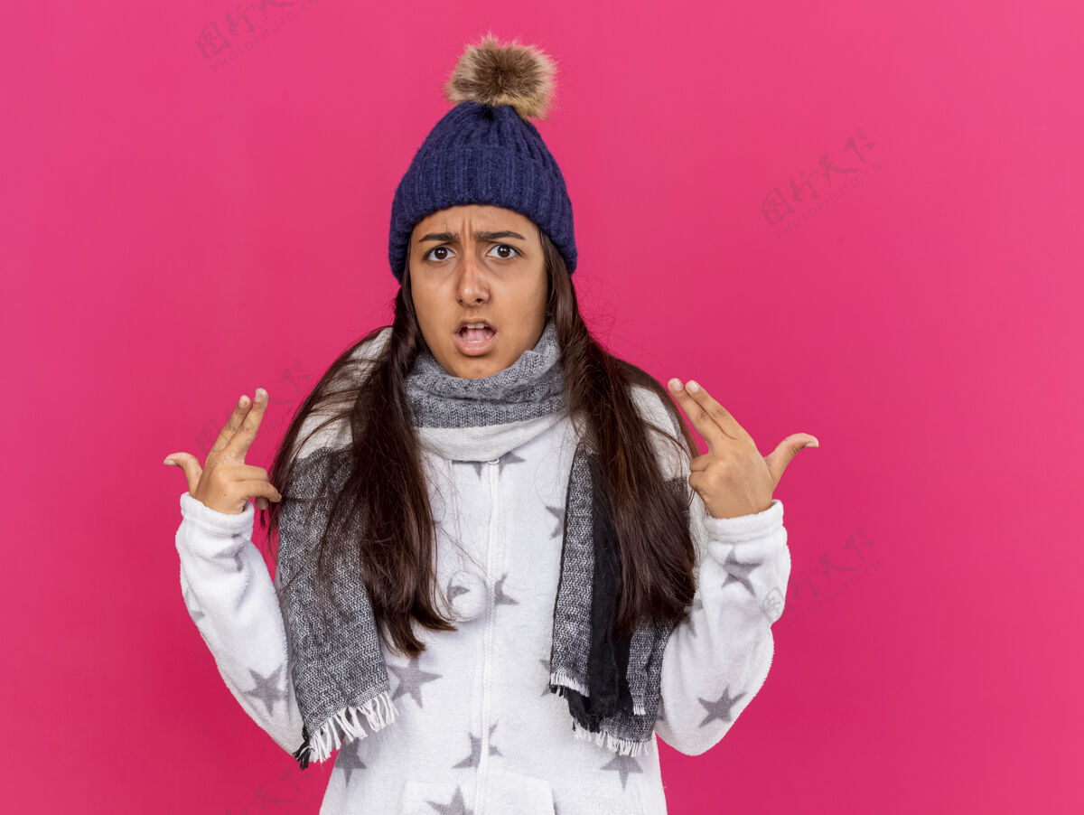 围巾戴着带围巾的冬季帽子的未出柜的生病小女孩指着自己 把自己孤立在粉红色的背景上她自己点女孩