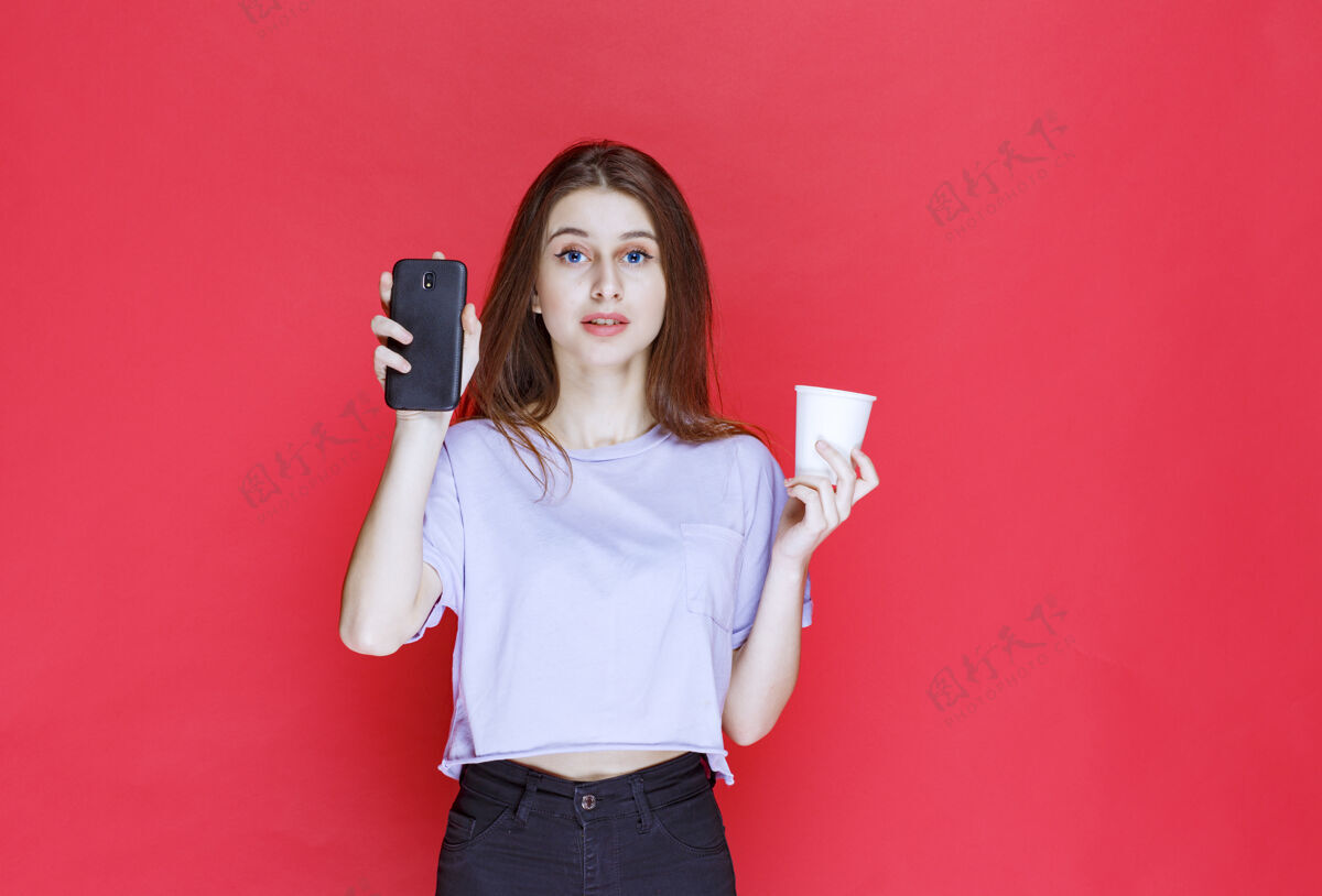 悲伤一个年轻女子拿着一杯饮料和一部黑色智能手机 脸上露出失望的表情电话纸杯水杯