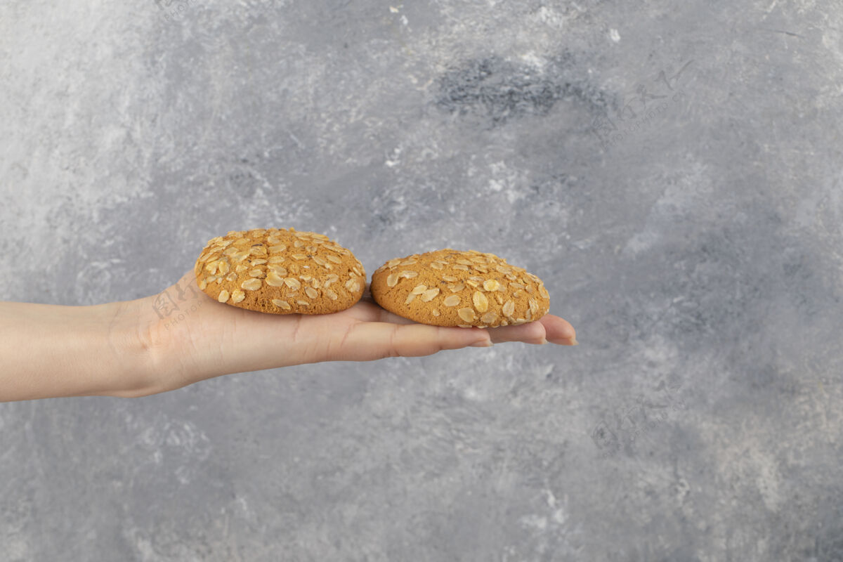 烘焙女人的手拿着两个燕麦片饼干在大理石表面燕麦脆面包屑