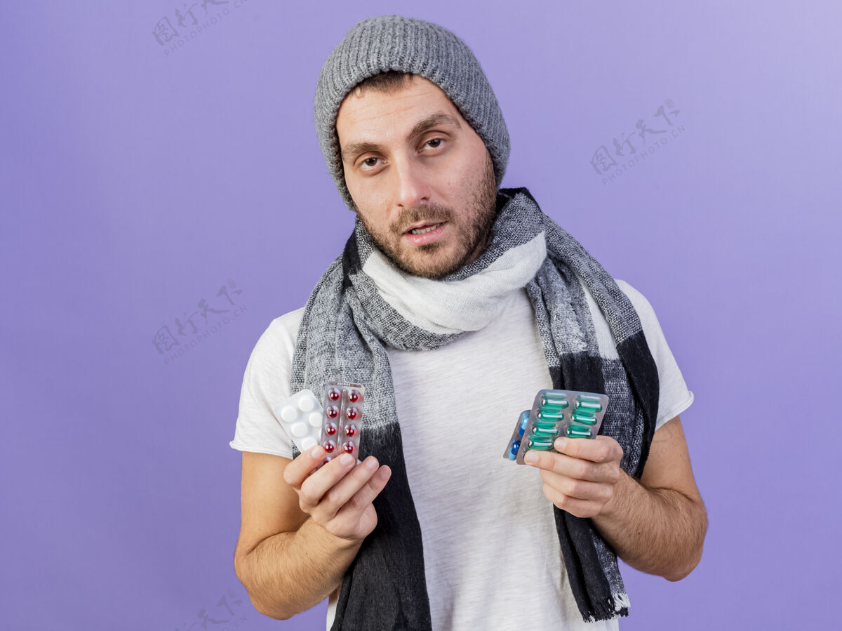 药片一个戴着冬天帽子 戴着围巾 拿着药丸的年轻人 被隔离在紫色的背景上围巾生病帽子