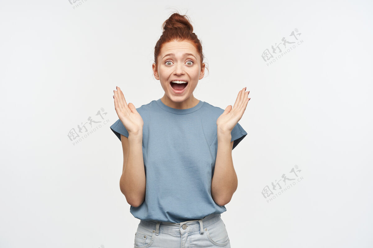 表情兴奋 快乐的女人 姜黄色的头发束成一个发髻穿着蓝色t恤和牛仔裤惊讶地抬起手掌情感概念隔着白墙成人女人轻