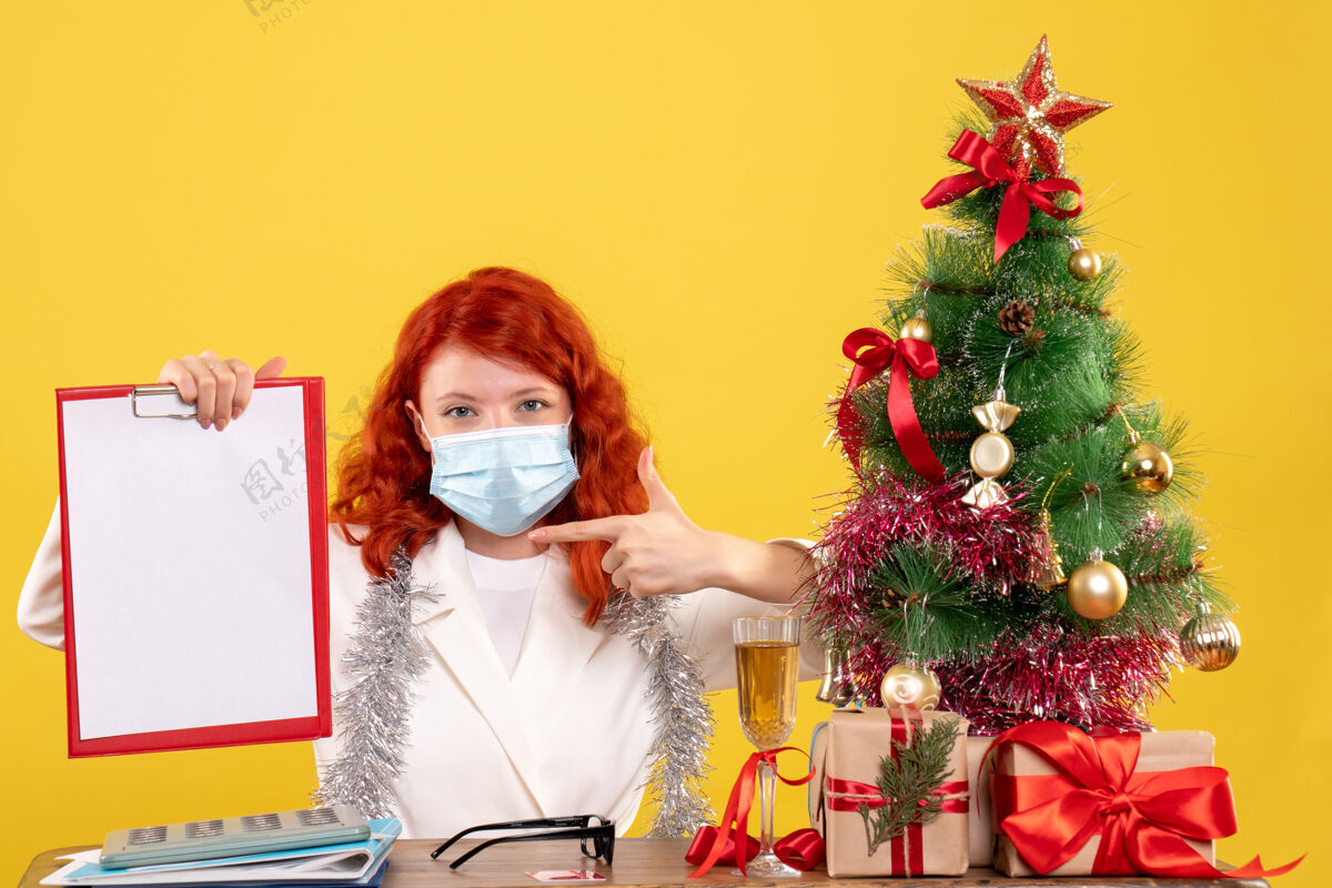 病毒前视图女医生围绕圣诞树和礼物坐在面具人年份周围