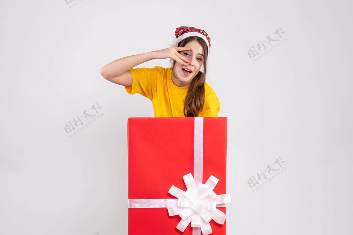 礼物前视图可爱的圣诞女孩与圣诞老人帽子站在背后大圣诞礼物丝带庆祝惊喜