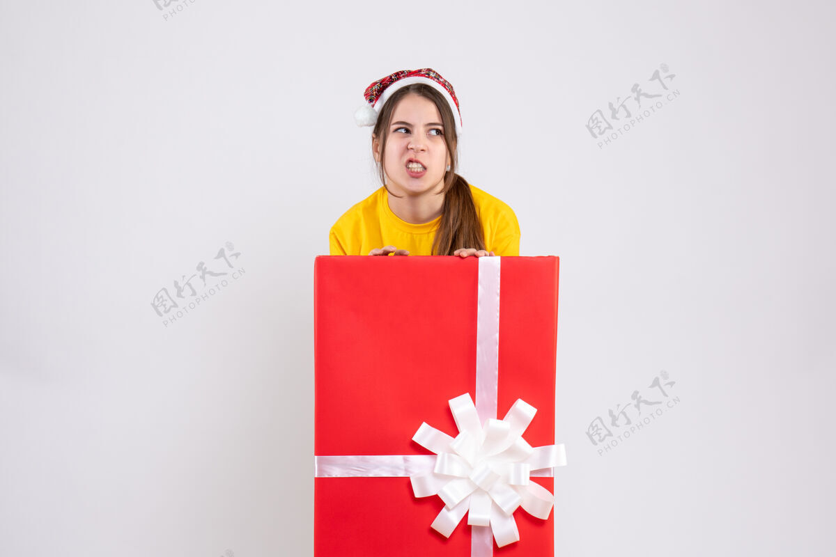 礼物前视图愤怒的女孩和圣诞老人帽子站在大礼物盒后面购物者站帽子