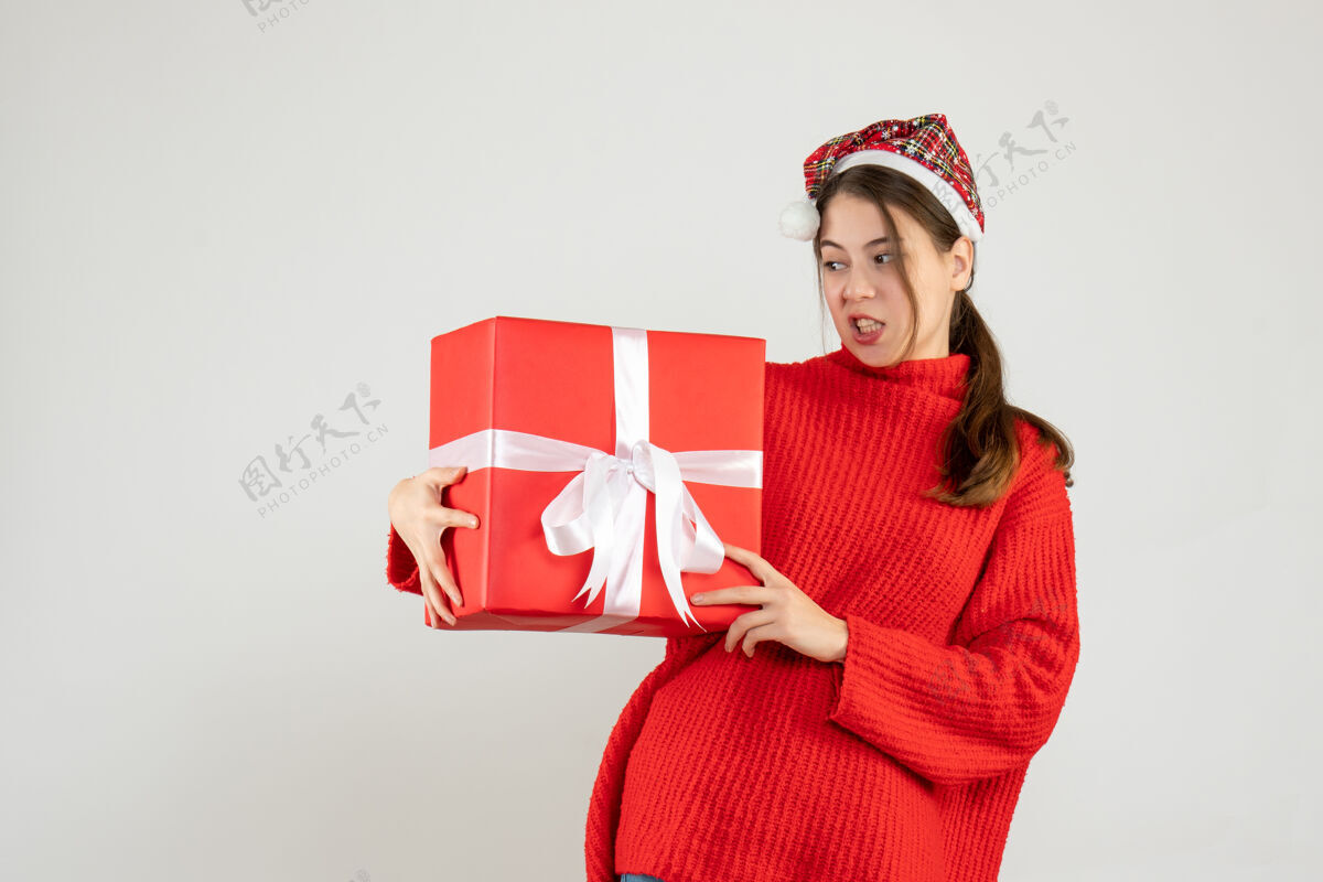 节日正面图不满戴圣诞帽的女孩举着礼物站着礼物不满意的女孩美丽
