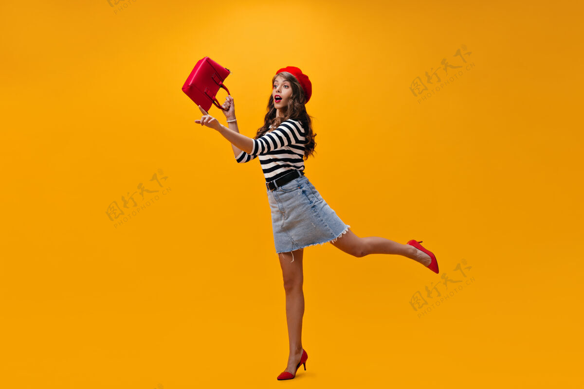 脸穿着时髦服装的女人在橙色的背景上奔跑拿着包穿着贝雷帽和条纹衬衫的年轻女孩摆出惊讶的姿势微笑紫色女人