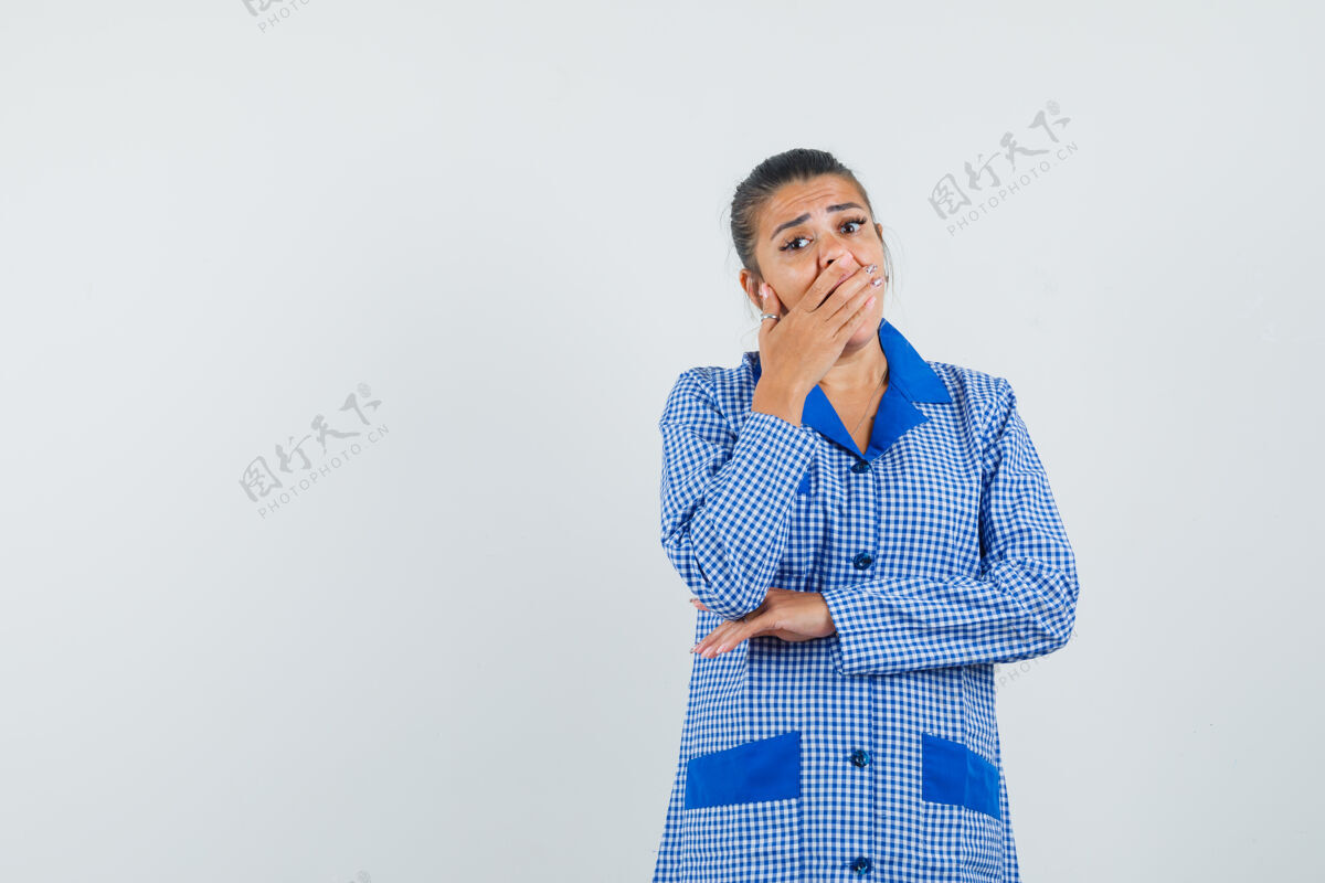 睡衣穿着蓝色方格睡衣衬衫的年轻女子用手捂住嘴 看上去很惊讶 正前方的景色时尚封面护理