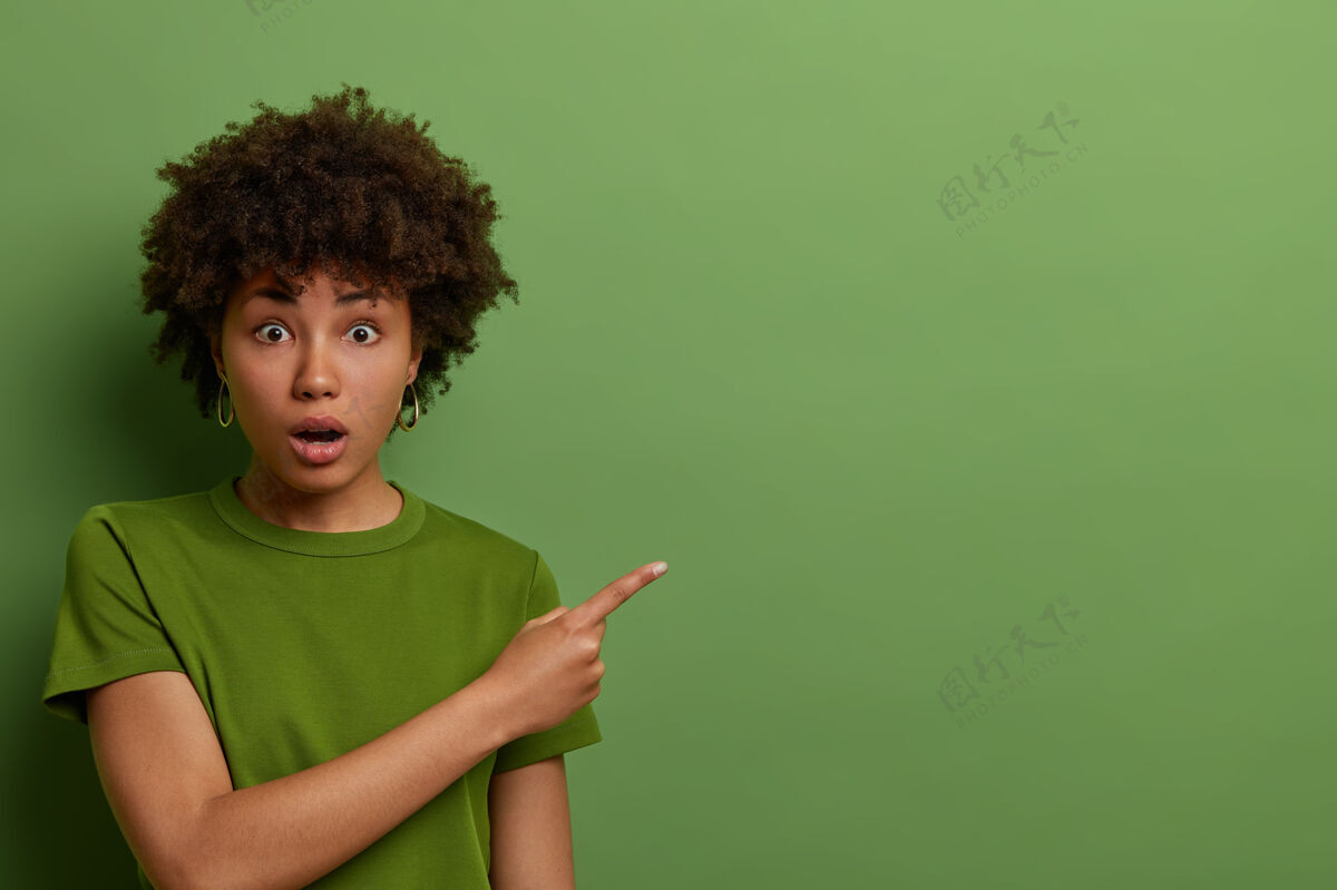 右惊讶兴奋的非裔美国妇女震惊地把食指放在一边 推销新产品 张大嘴巴看广告 穿着同一色调的亮绿色t恤非洲惊人卷发