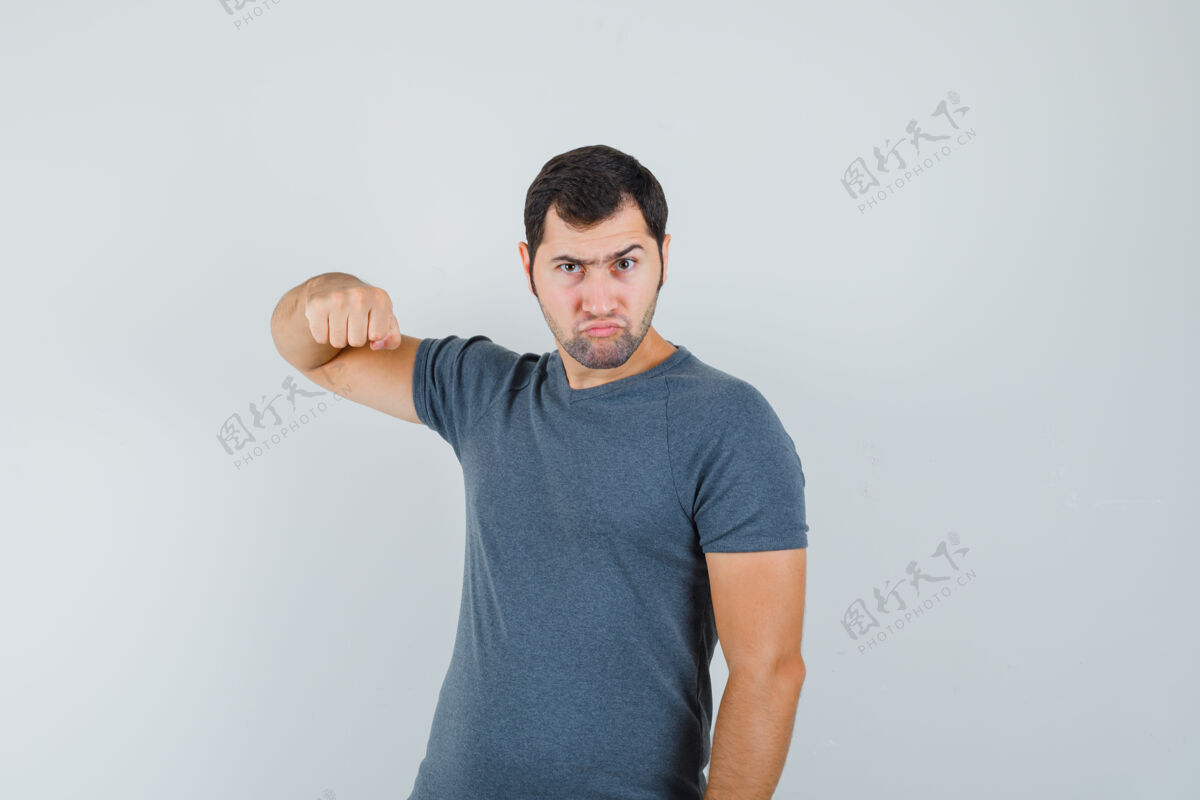 男孩穿着灰色t恤的年轻男子用拳头威胁 看上去很紧张小接听电话远观