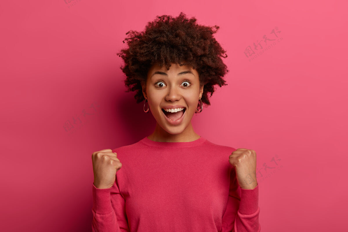 高兴成功的甜味积极快乐的黑皮肤女人举起紧握的拳头 取得成功 积极地惊呼 喊是的 为胜利欢呼 高兴地成为冠军 孤立在粉红色的墙上女人情绪最好的