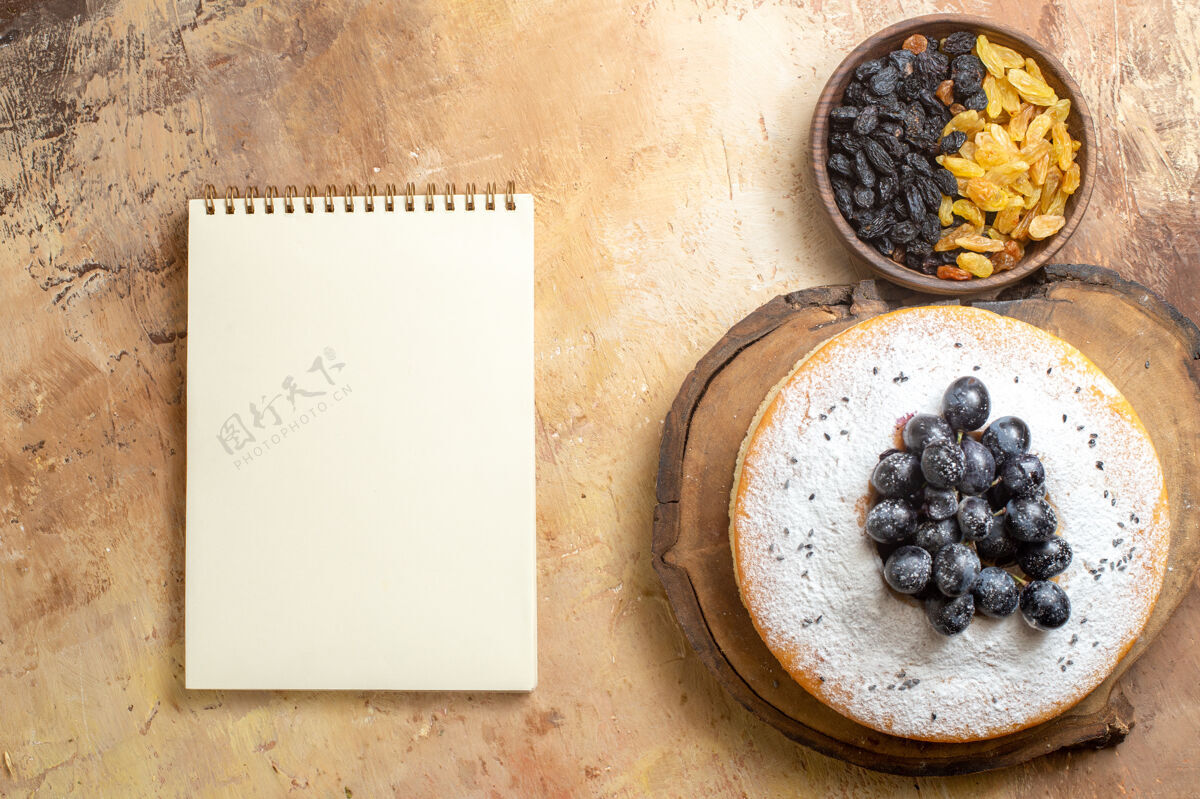 特写顶视图葡萄干绿色和黑色葡萄干在碗蛋糕与葡萄糖白色笔记本葡萄早餐蛋糕