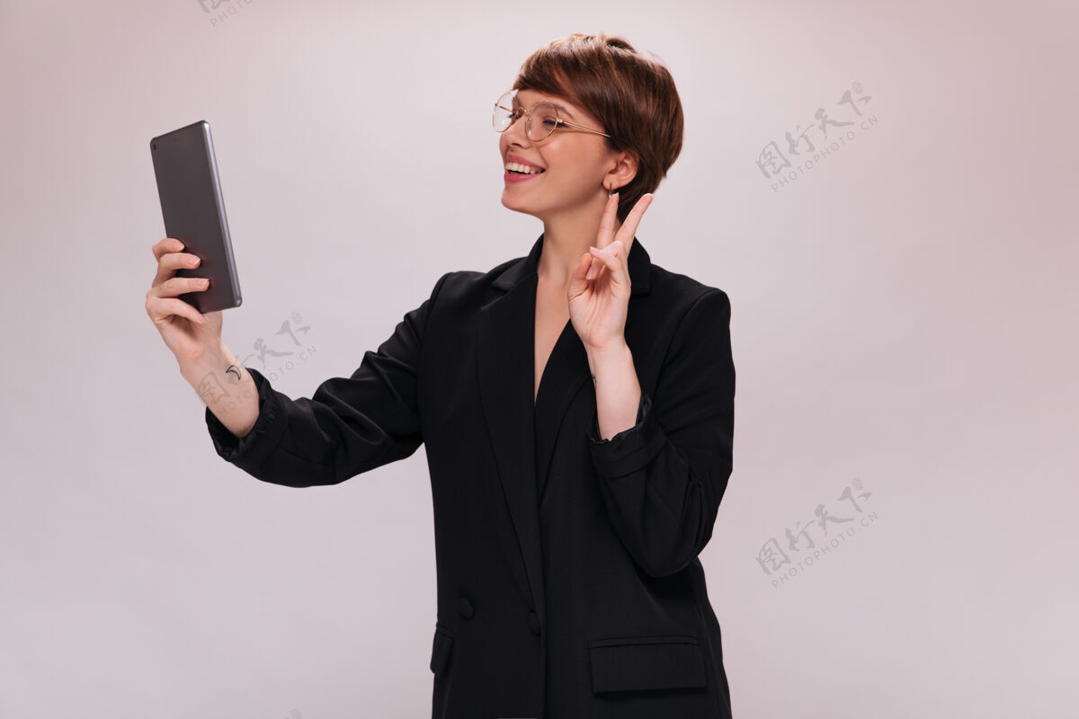 站立身着黑色西装的快乐女士手持平板电脑 在与世隔绝的背景下自拍身着夹克的快乐女士在白色背景下微笑成人女士单身