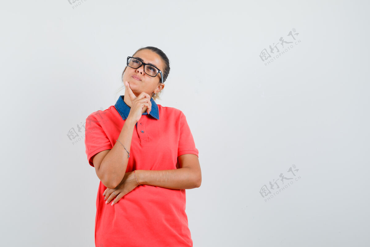 护理年轻女子站在思考的姿势在红色t恤衫和眼镜 并期待沉思前视图漂亮站模特