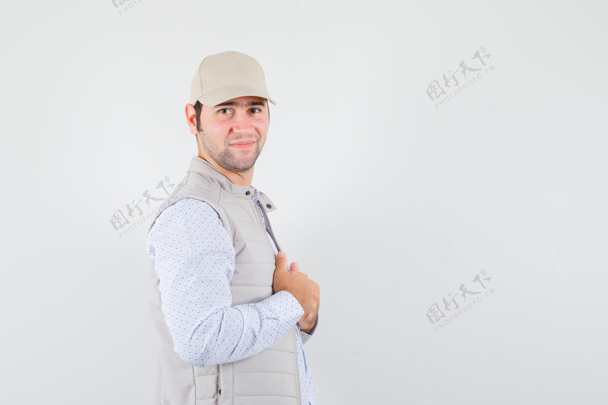 男性年轻人调整着衣领 穿着衬衫 无袖夹克 戴着帽子 看上去很自信人热姿势