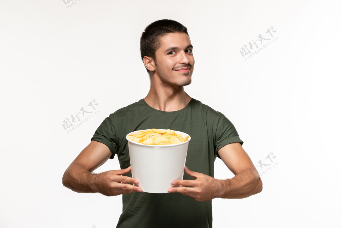 电影正面图身穿绿色t恤的年轻男性 白色地板上有土豆cips 孤独的人杯子土豆电影