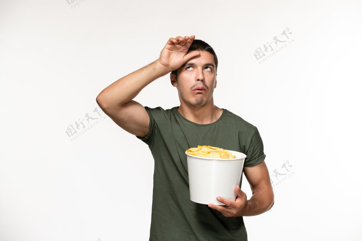 杯子正面图身穿绿色t恤的年轻男子手持土豆cips在白墙上孤独的人电影早餐电影咖啡