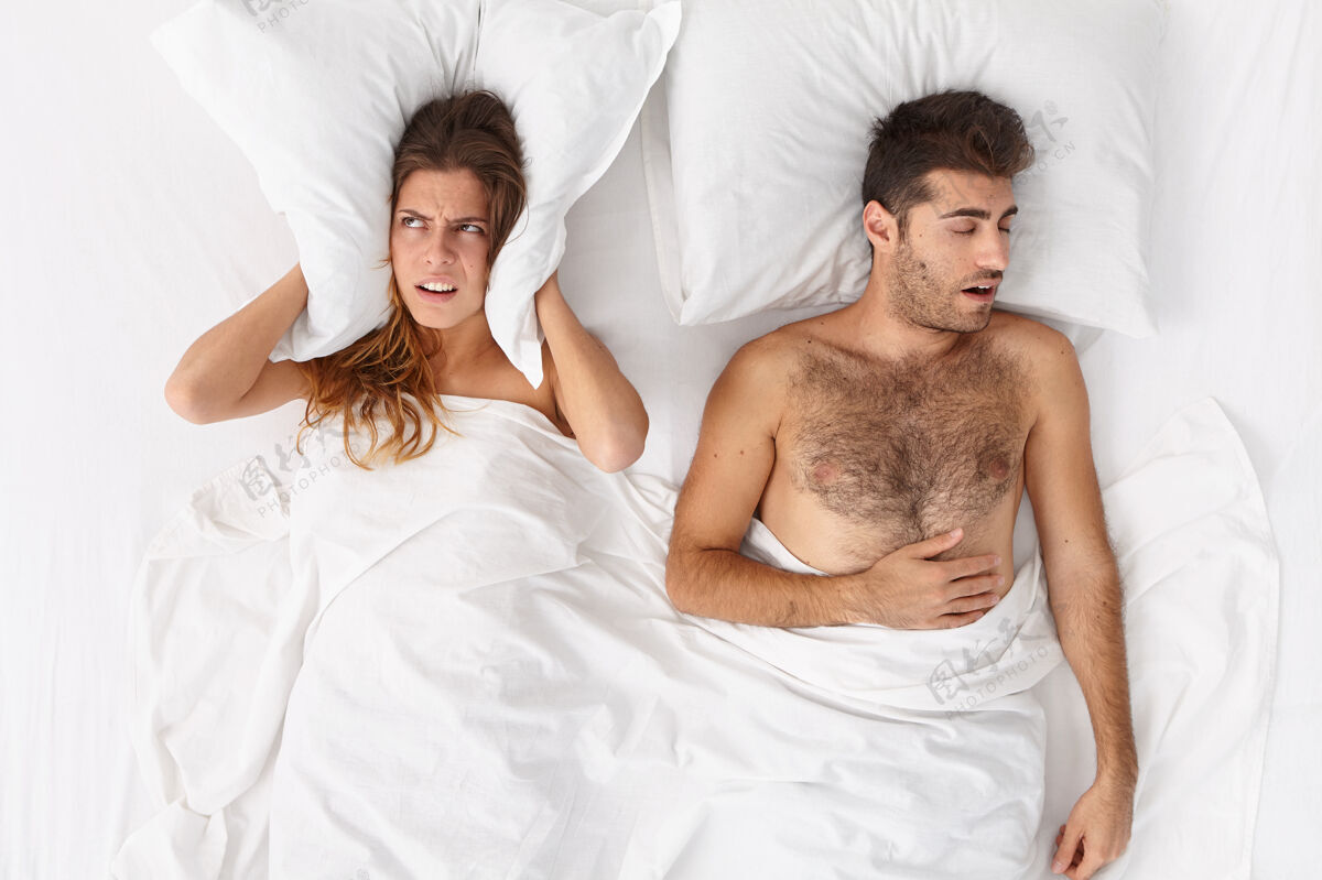卧室夫妻在床上抑郁的年轻女子用枕头捂住耳朵 因为男人打鼾睡不着觉 失眠 躺在床上烦躁家庭 睡觉时间 失眠 睡眠问题概念不高兴舒适坏