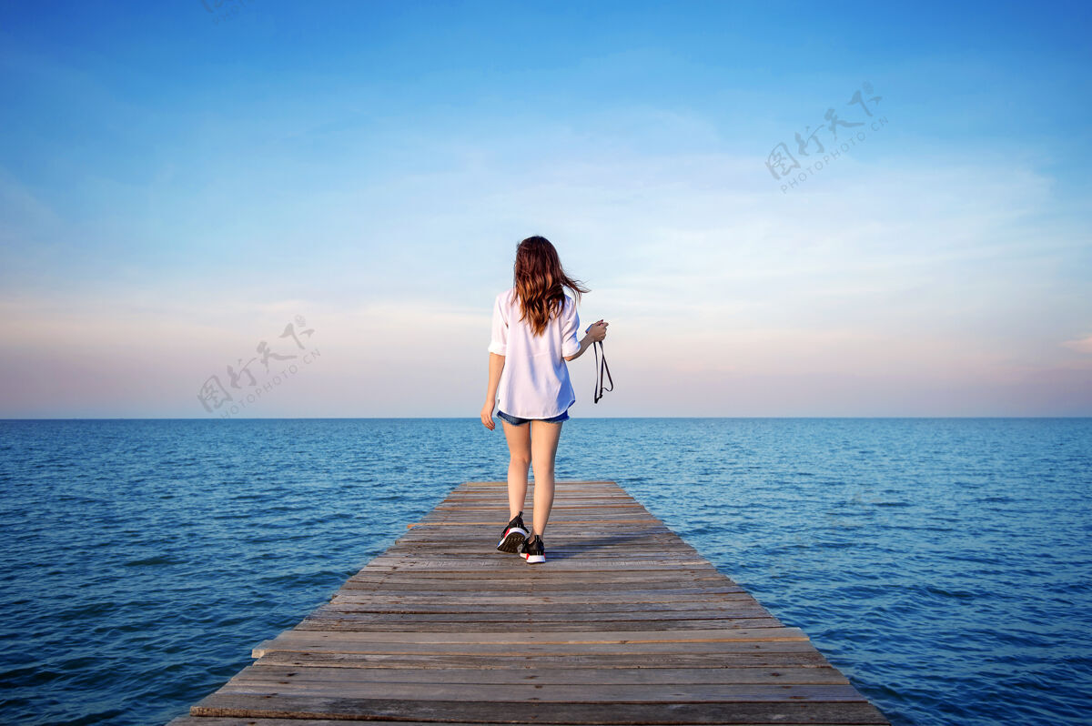 自然走在木桥上的女人伸进了大海日落异国情调服装