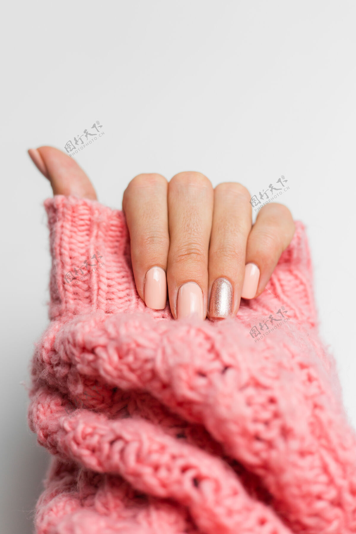 工艺漂亮的裸色美甲 一个手指闪亮的金色 在针织粉色羊毛枕头的背景下健康治疗皮肤