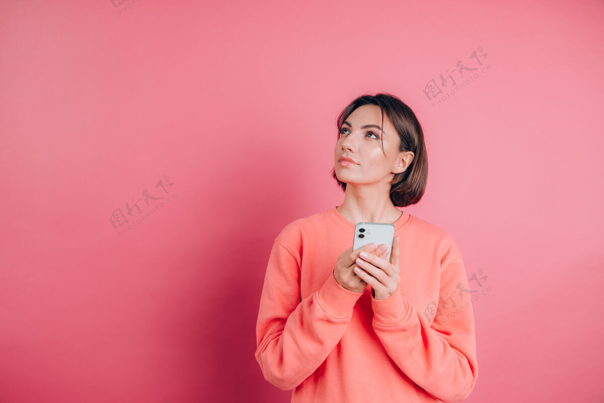 思考想着梦中的年轻漂亮女人用手机在粉色的墙壁背景上孤零零地摆姿势高兴粉色一个