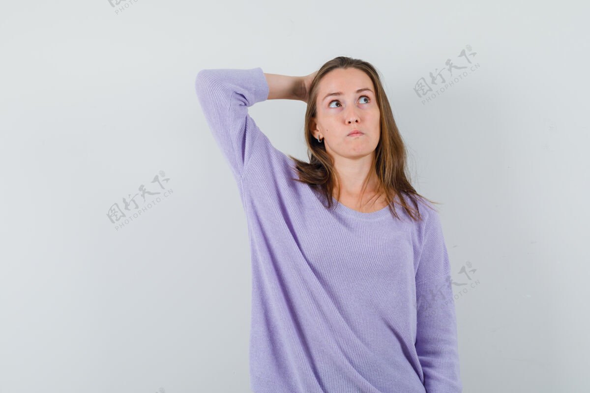 自信年轻的女性手拉在脑后 一边看着淡紫色衬衫 一边沉思着衬衫卷发头发