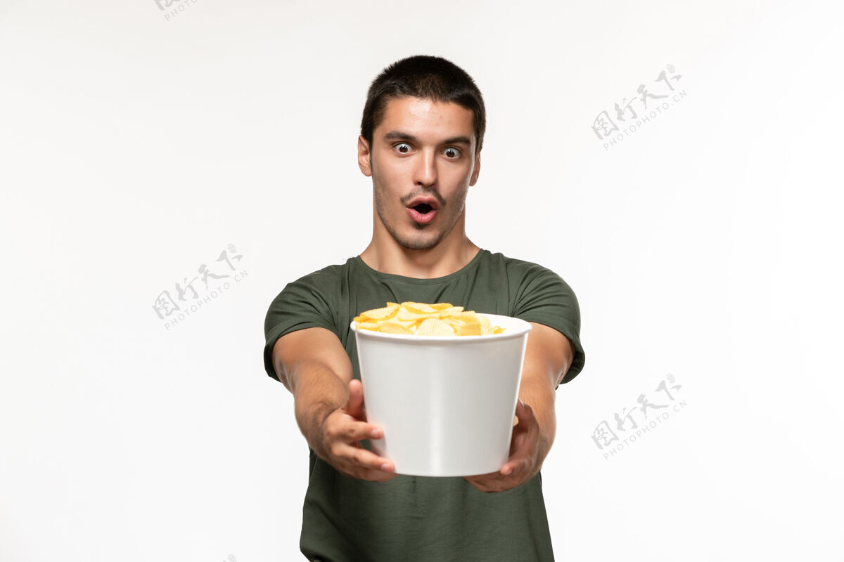 杯子正面图身穿绿色t恤的年轻男子手持土豆cips站在白墙上孤独的电影人土豆电影电影