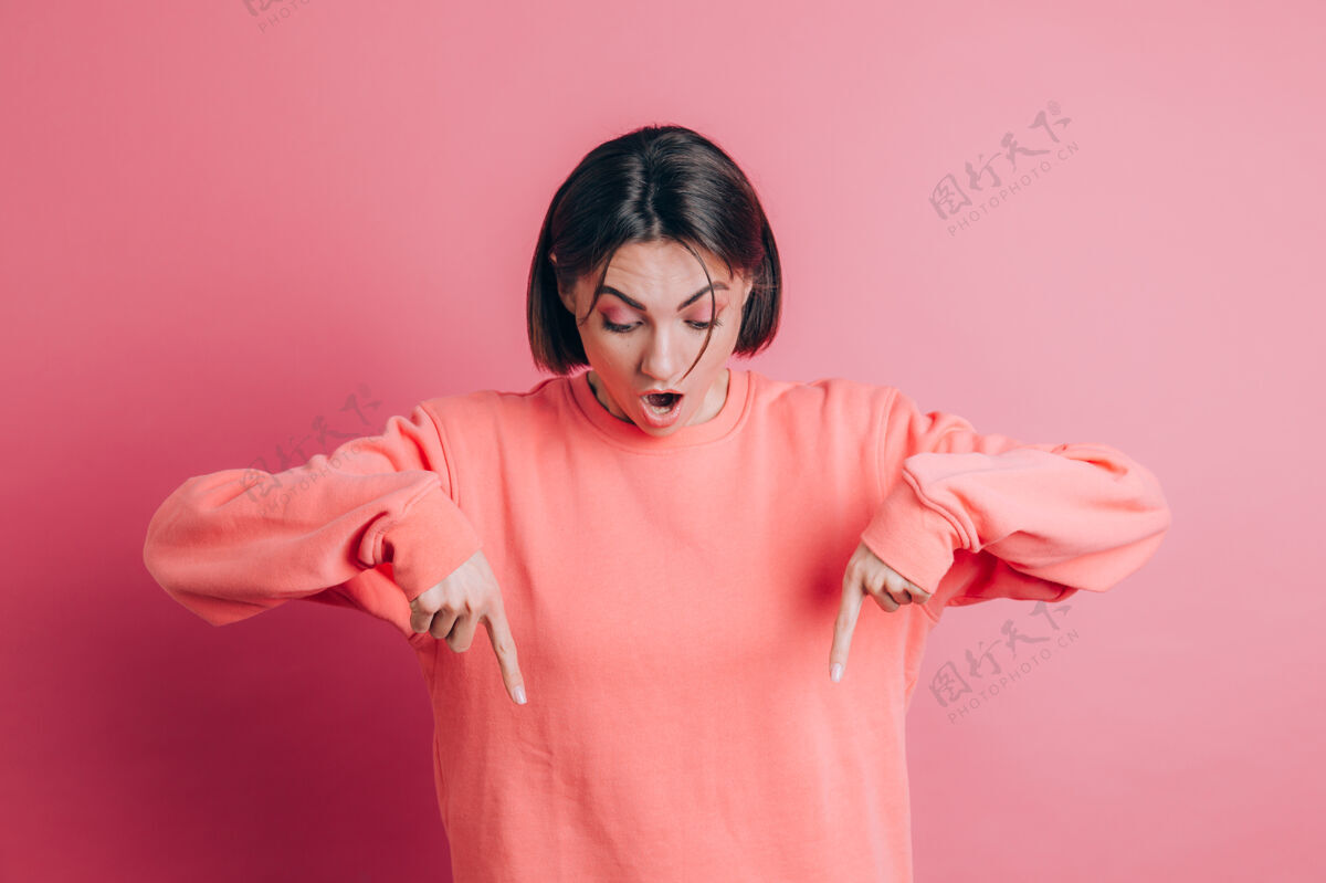 空间背景上穿着休闲毛衣的女人手指朝下 露出广告 惊讶的脸和张开的嘴站立向下积极